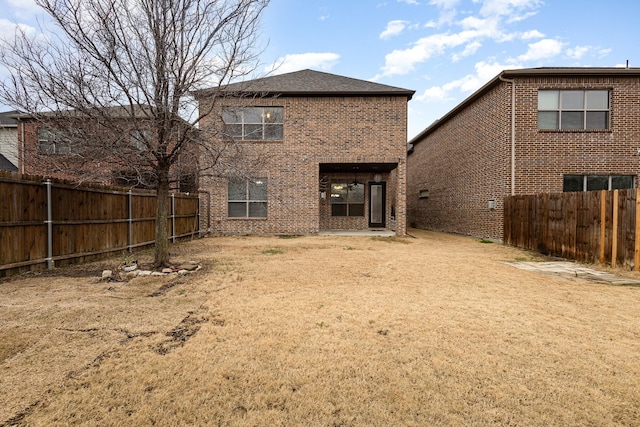 back of house with a fenced backyard, brick siding, and a lawn