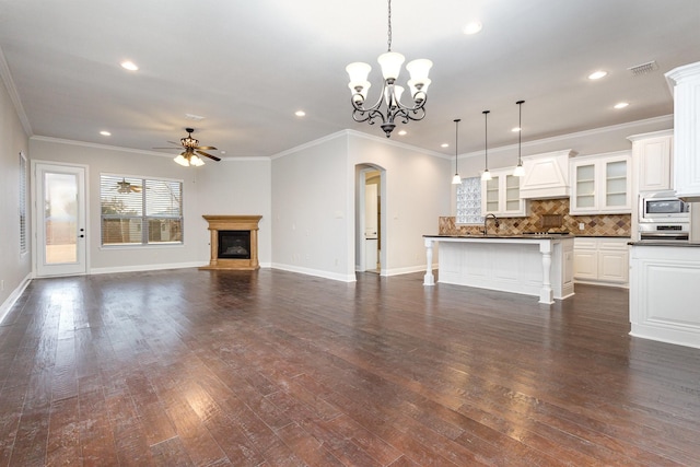 unfurnished living room featuring arched walkways, ceiling fan with notable chandelier, visible vents, dark wood finished floors, and a glass covered fireplace