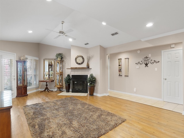 living room with hardwood / wood-style flooring, ceiling fan, lofted ceiling, and a tiled fireplace