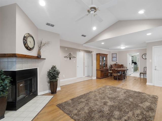 living room featuring lofted ceiling, a tiled fireplace, ornamental molding, ceiling fan, and light hardwood / wood-style flooring