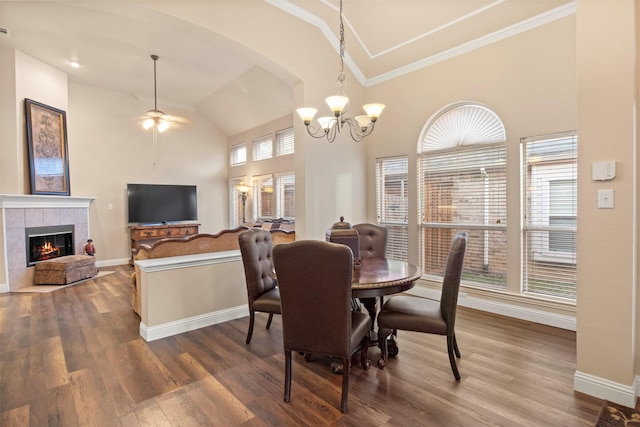 dining area featuring high vaulted ceiling, ornamental molding, hardwood / wood-style flooring, a fireplace, and ceiling fan with notable chandelier