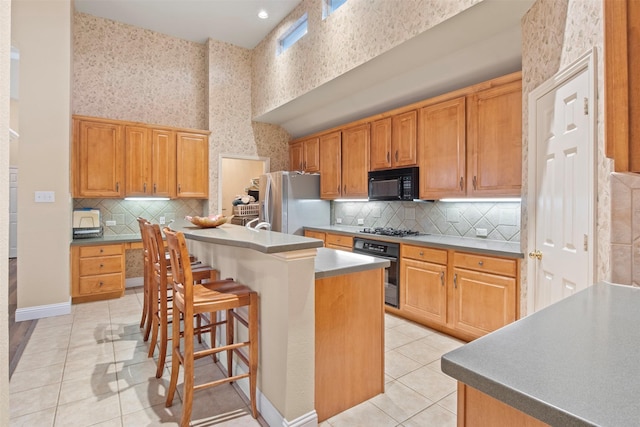 kitchen with light tile patterned flooring, a kitchen breakfast bar, a kitchen island, a towering ceiling, and black appliances