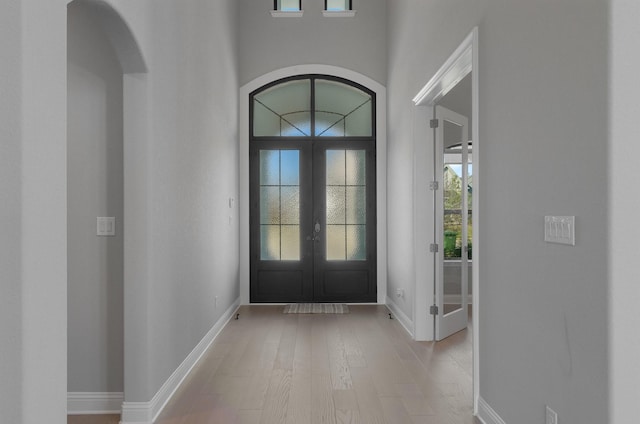 foyer featuring a towering ceiling, french doors, and light wood-type flooring