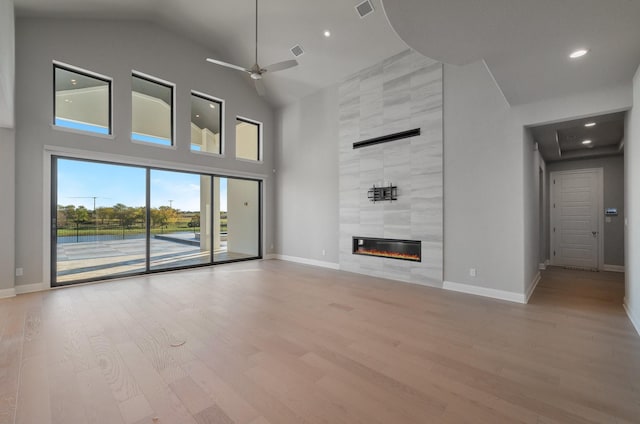 unfurnished living room with ceiling fan, light hardwood / wood-style floors, a tile fireplace, and a towering ceiling