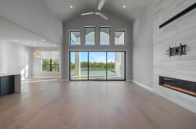 unfurnished living room featuring a high ceiling, a tile fireplace, ceiling fan with notable chandelier, and light wood-type flooring