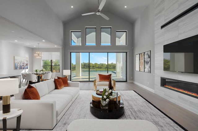 living room with ceiling fan with notable chandelier, a fireplace, high vaulted ceiling, and light wood-type flooring