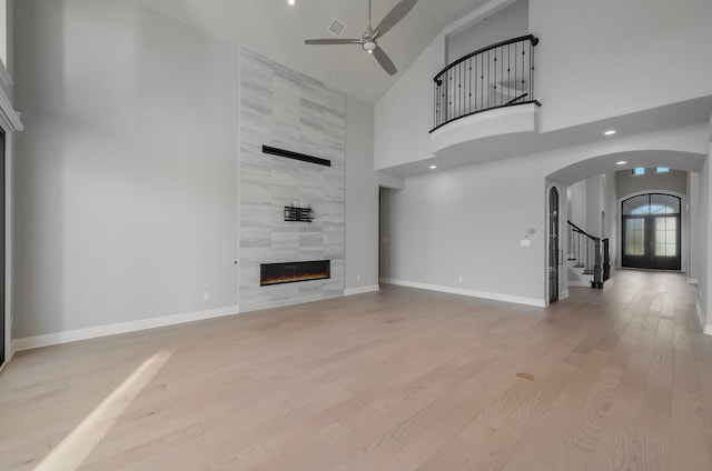 unfurnished living room featuring ceiling fan, high vaulted ceiling, light wood-type flooring, and a fireplace