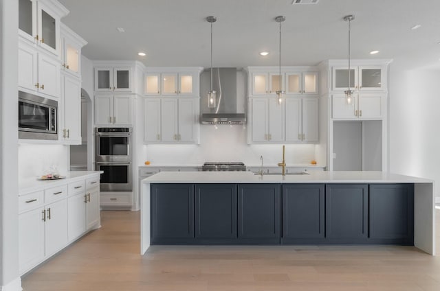 kitchen with white cabinetry, stainless steel appliances, an island with sink, and wall chimney exhaust hood