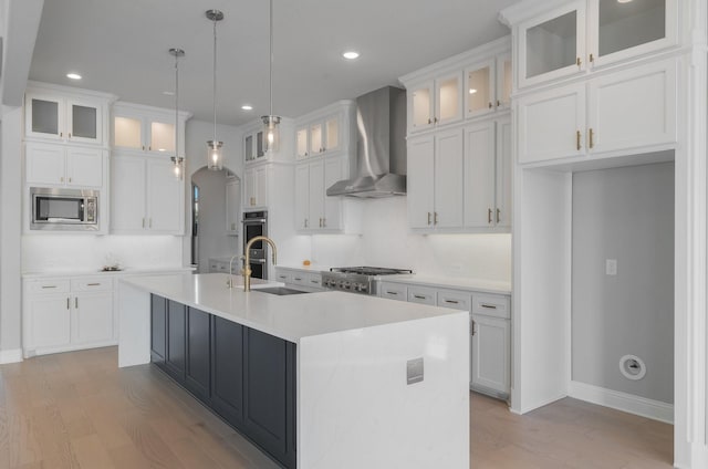 kitchen featuring white cabinets, stainless steel appliances, an island with sink, and wall chimney exhaust hood