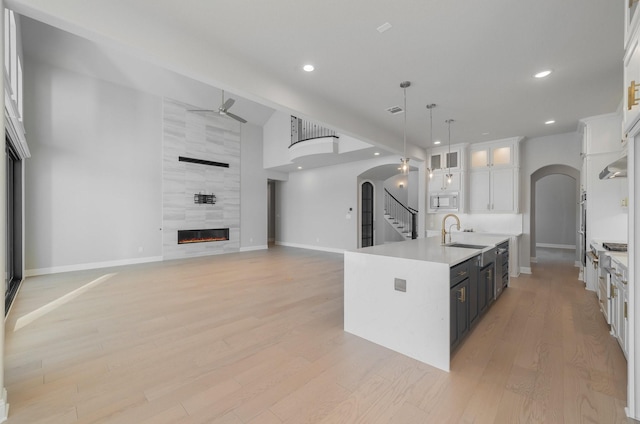 kitchen with a fireplace, decorative light fixtures, white cabinetry, sink, and a kitchen island with sink