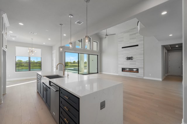 kitchen featuring hanging light fixtures, stainless steel dishwasher, a fireplace, and light hardwood / wood-style floors