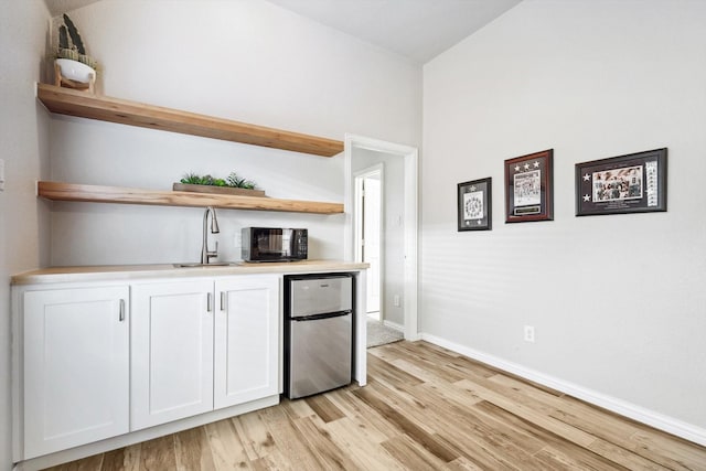 bar with white cabinetry, sink, stainless steel refrigerator, and light hardwood / wood-style floors