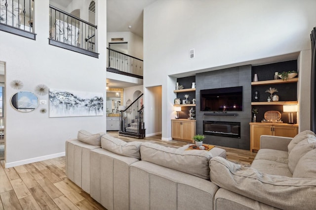 living room featuring a tile fireplace, a towering ceiling, built in features, and light hardwood / wood-style floors