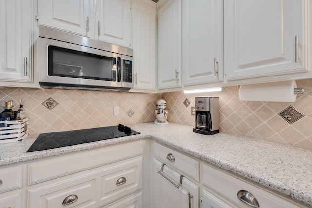 kitchen with white cabinetry, light stone countertops, black electric cooktop, and decorative backsplash