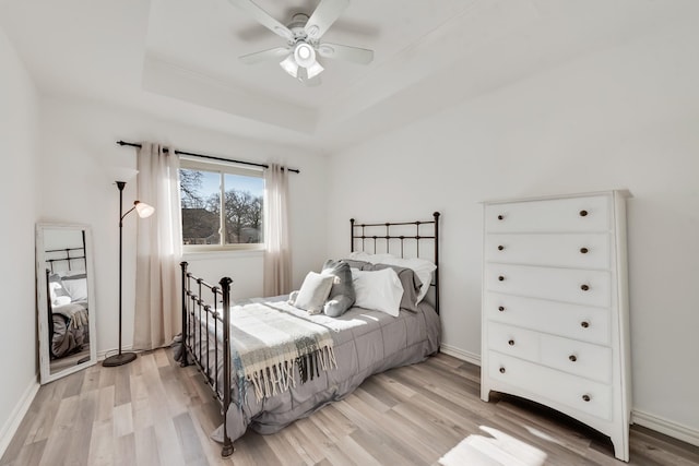 bedroom featuring ceiling fan, a raised ceiling, and light hardwood / wood-style floors