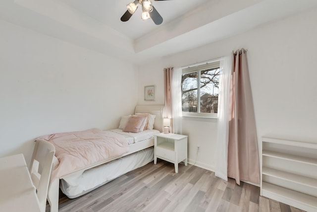 bedroom featuring light wood-type flooring, ceiling fan, and a tray ceiling