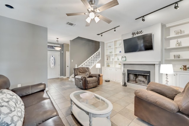 living room featuring light tile patterned floors, built in features, rail lighting, a tile fireplace, and ceiling fan