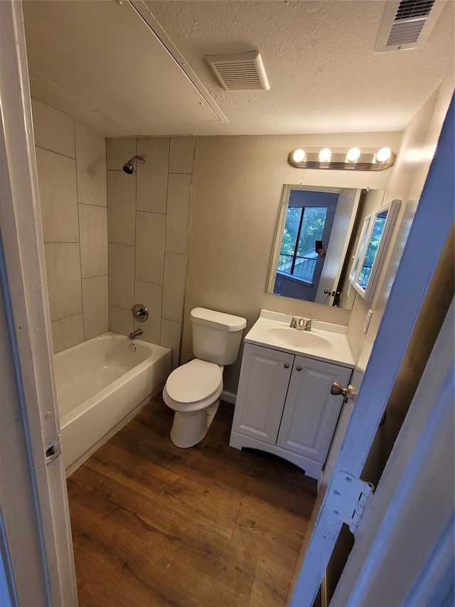 full bathroom with tiled shower / bath, hardwood / wood-style flooring, vanity, toilet, and a textured ceiling