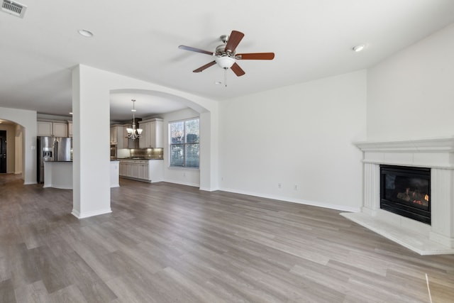 unfurnished living room featuring ceiling fan with notable chandelier and light hardwood / wood-style floors