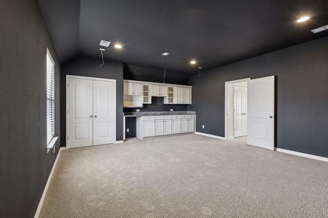 kitchen with vaulted ceiling, light carpet, and white cabinets