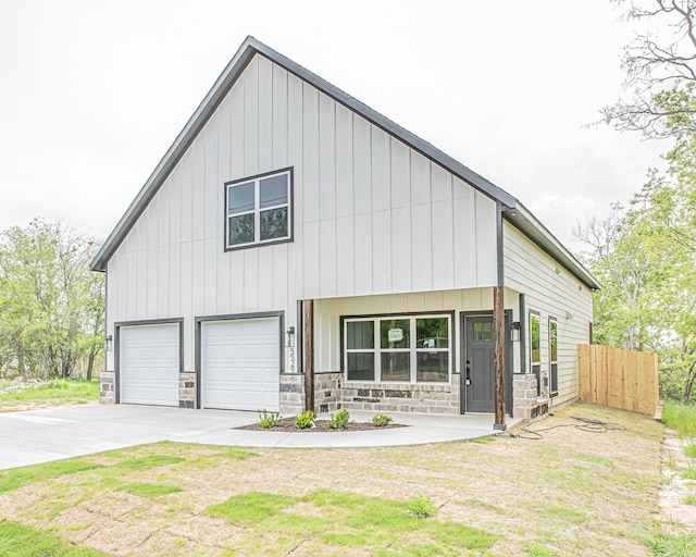 modern farmhouse style home with fence, concrete driveway, an attached garage, board and batten siding, and stone siding