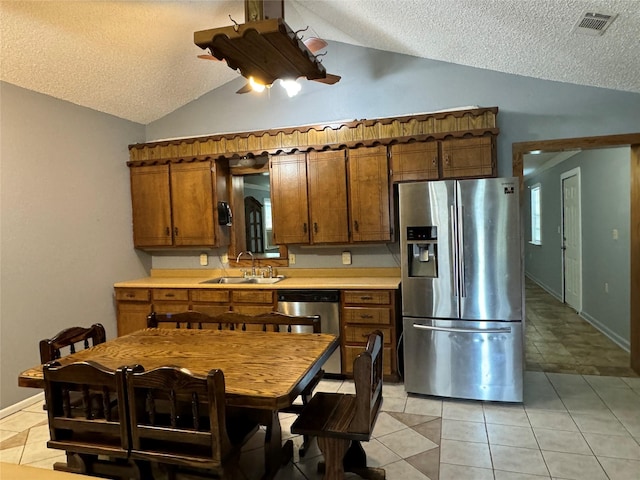 kitchen featuring sink, appliances with stainless steel finishes, a textured ceiling, light tile patterned flooring, and vaulted ceiling