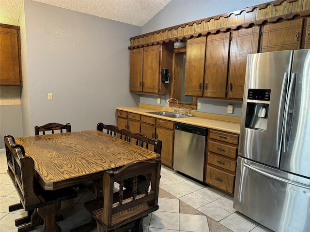 kitchen featuring sink, vaulted ceiling, a textured ceiling, light tile patterned floors, and stainless steel appliances