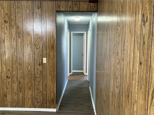 hallway with dark wood-type flooring, a textured ceiling, and wood walls