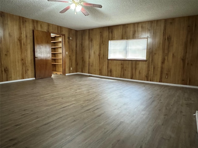 spare room featuring dark wood-type flooring, ceiling fan, a textured ceiling, and wood walls