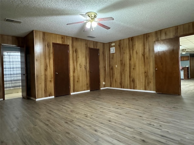 spare room with hardwood / wood-style flooring, ceiling fan, a textured ceiling, and wood walls