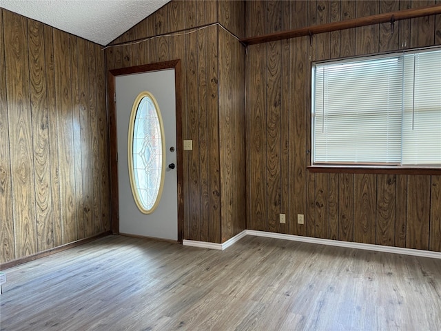 entryway featuring wood walls, lofted ceiling, a textured ceiling, and light hardwood / wood-style flooring