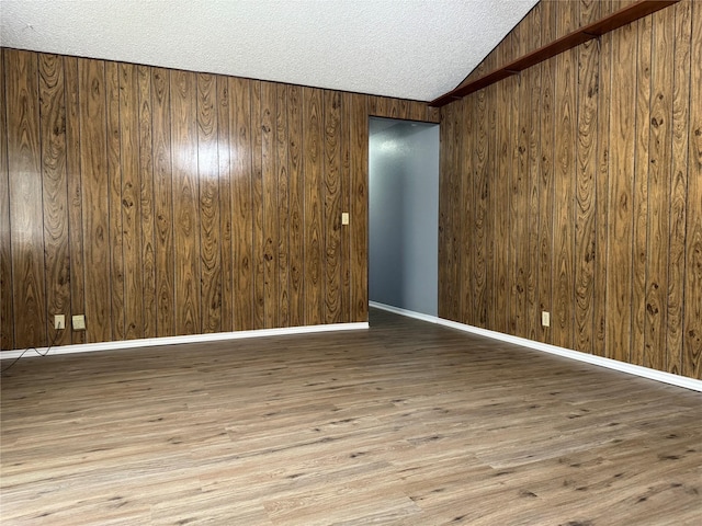 spare room featuring vaulted ceiling, a textured ceiling, light hardwood / wood-style flooring, and wood walls