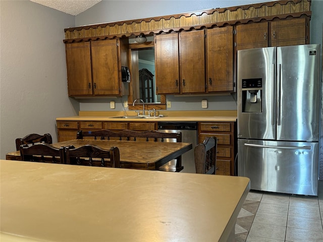 kitchen with lofted ceiling, sink, light tile patterned floors, stainless steel appliances, and a textured ceiling