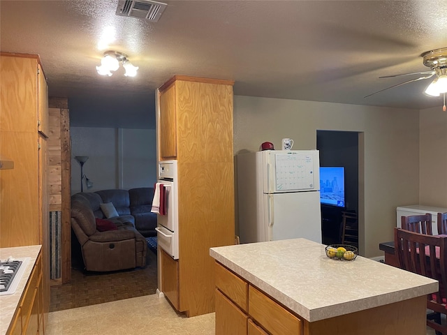 kitchen featuring ceiling fan, white appliances, a kitchen island, and a textured ceiling