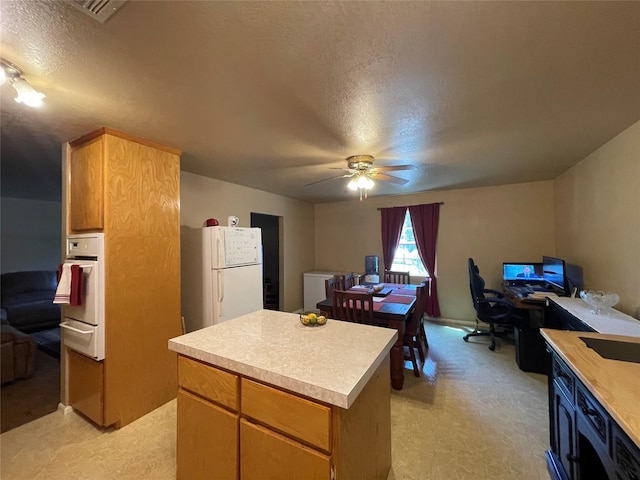 kitchen with ceiling fan, white appliances, a textured ceiling, and a kitchen island