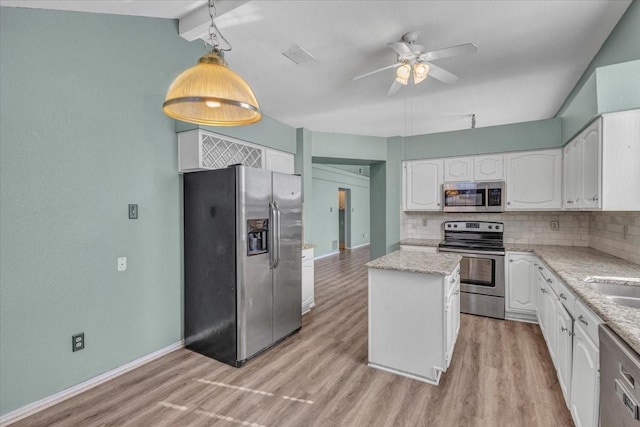 kitchen with appliances with stainless steel finishes, tasteful backsplash, light stone countertops, a kitchen island, and decorative light fixtures