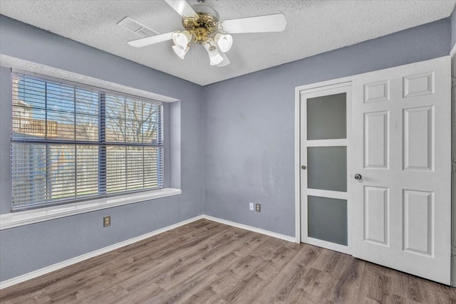 unfurnished bedroom with multiple windows, a textured ceiling, wood-type flooring, and ceiling fan