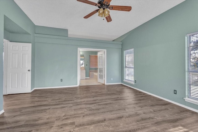 spare room with lofted ceiling, a healthy amount of sunlight, hardwood / wood-style floors, and a textured ceiling