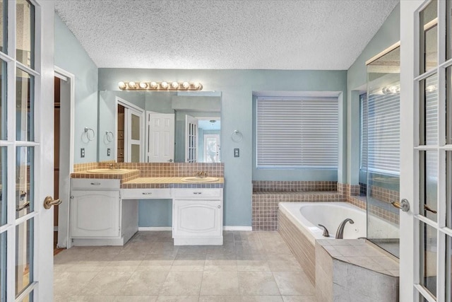 bathroom with vanity, a relaxing tiled tub, tile patterned floors, a textured ceiling, and french doors