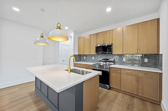 kitchen featuring pendant lighting, sink, stainless steel appliances, a center island with sink, and light wood-type flooring