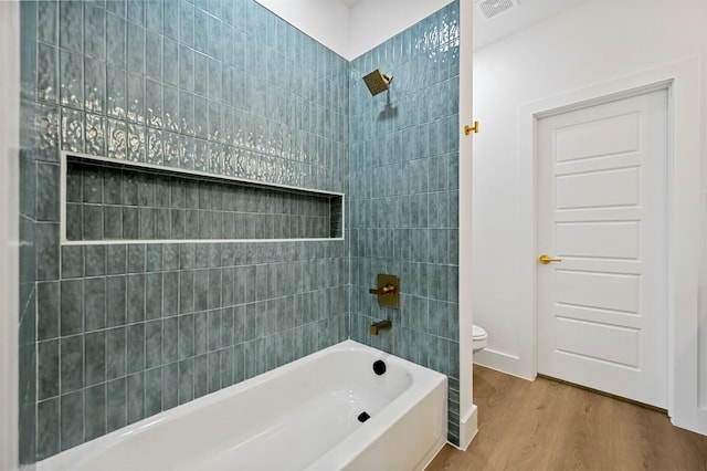 bathroom with tiled shower / bath combo, wood-type flooring, and toilet