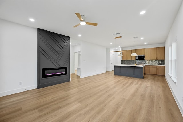 kitchen with hanging light fixtures, an island with sink, a fireplace, and light hardwood / wood-style flooring