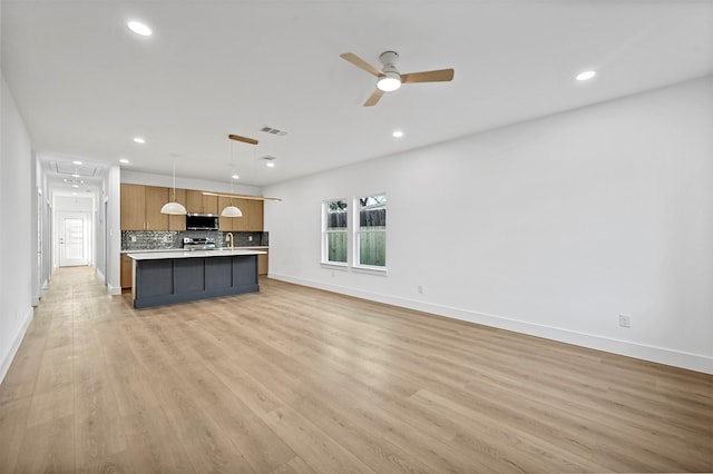 kitchen featuring pendant lighting, an island with sink, backsplash, stainless steel appliances, and light hardwood / wood-style flooring