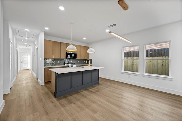 kitchen featuring decorative light fixtures, a center island with sink, stainless steel appliances, light hardwood / wood-style floors, and decorative backsplash