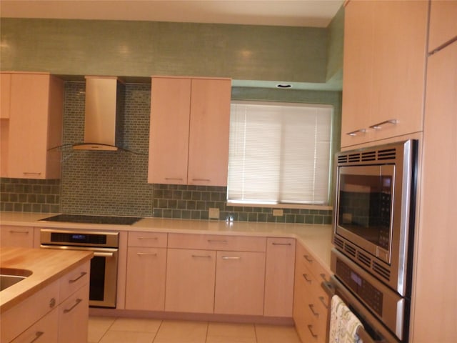 kitchen featuring tasteful backsplash, appliances with stainless steel finishes, wall chimney range hood, and light brown cabinets