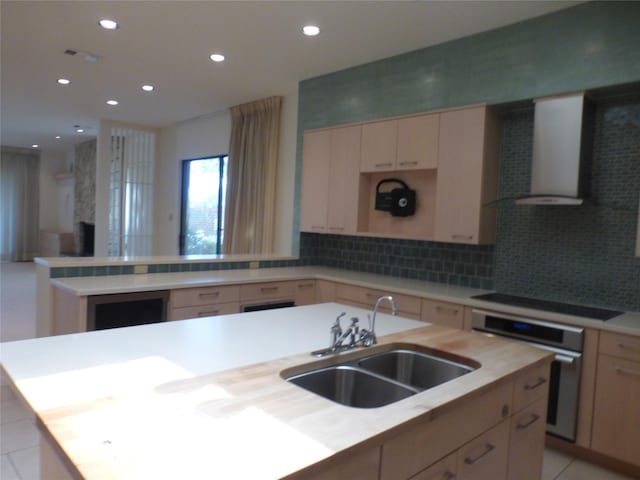 kitchen featuring sink, tasteful backsplash, an island with sink, oven, and wall chimney exhaust hood