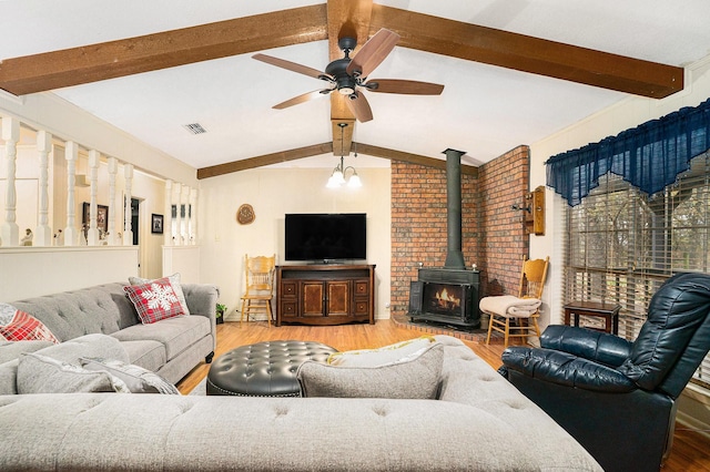 living room with light hardwood / wood-style flooring, lofted ceiling with beams, ceiling fan, and a wood stove