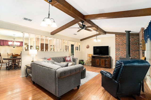 living room with hardwood / wood-style floors, ceiling fan with notable chandelier, lofted ceiling with beams, and a wood stove