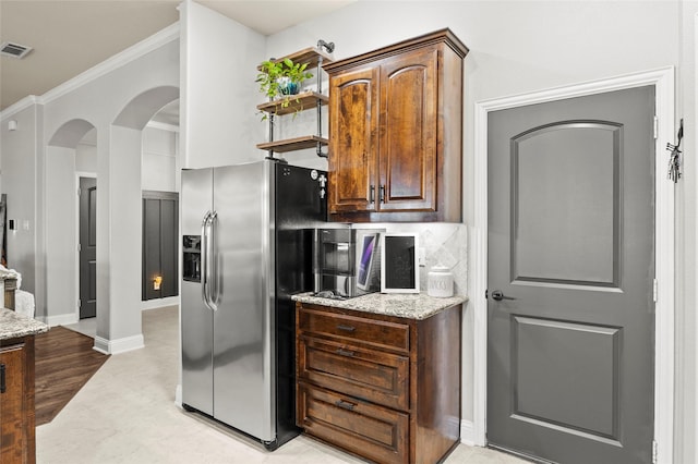 kitchen with stainless steel refrigerator with ice dispenser, crown molding, light stone counters, and decorative backsplash