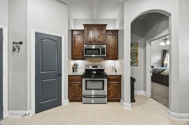 kitchen featuring tasteful backsplash, stainless steel appliances, light stone countertops, and dark brown cabinets